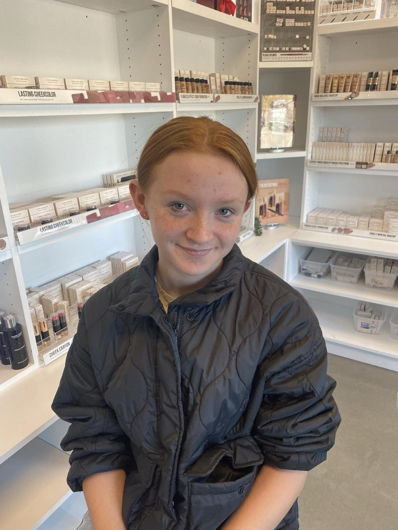 A young girl in a black jacket is sitting in a store.