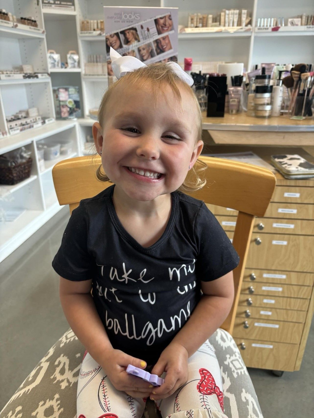 A little girl is sitting in a chair with a card in her hair.
