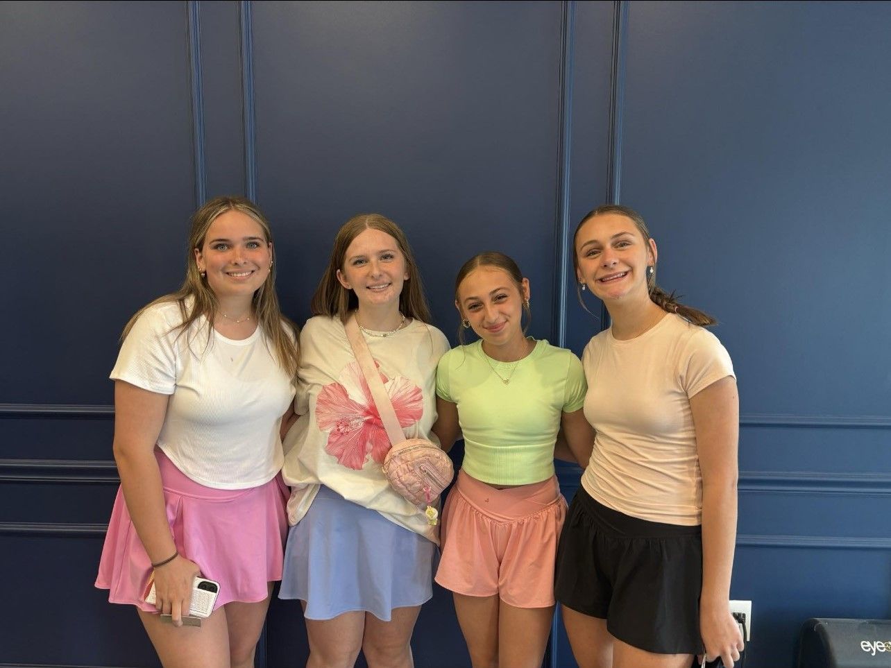 A group of young women are posing for a picture in front of a blue wall.