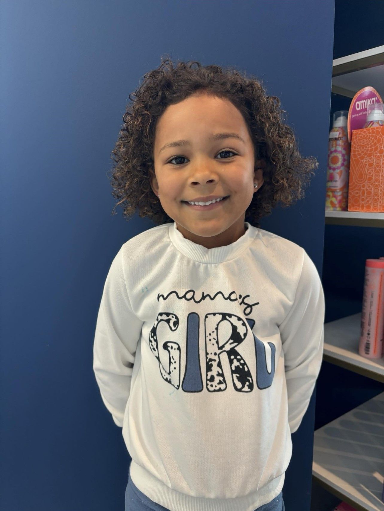 A little girl wearing a white shirt that says mamas girl