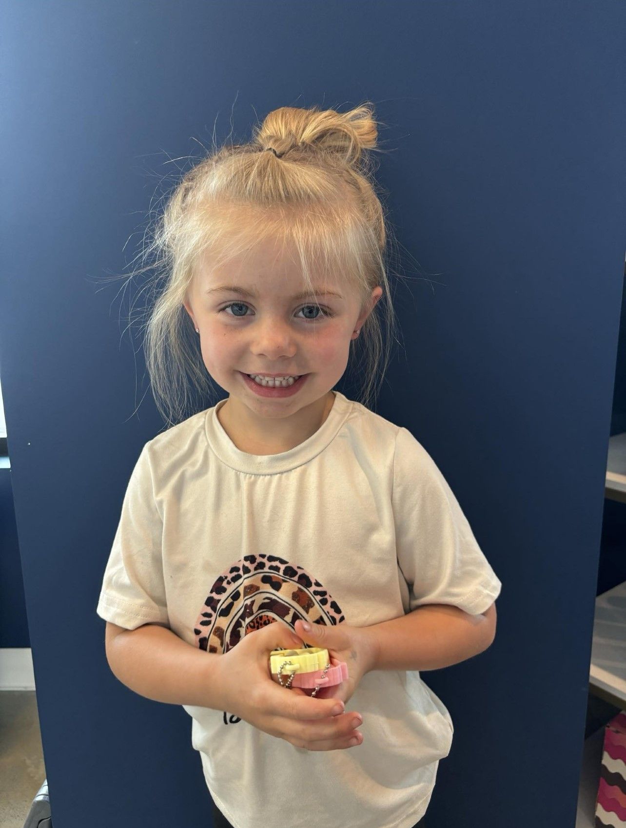 A little girl in a white shirt is holding a yellow object in her hands.