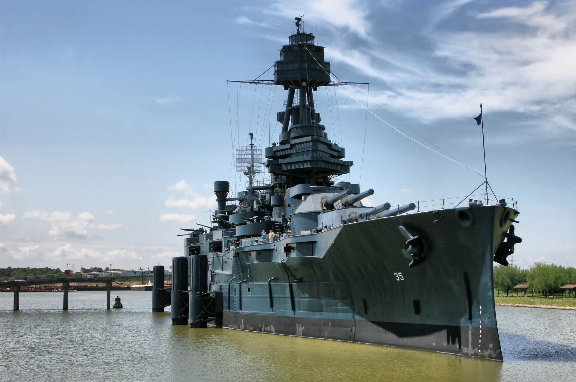 Battleship Texas, grey warship, docked in water, sunny day, blue sky.