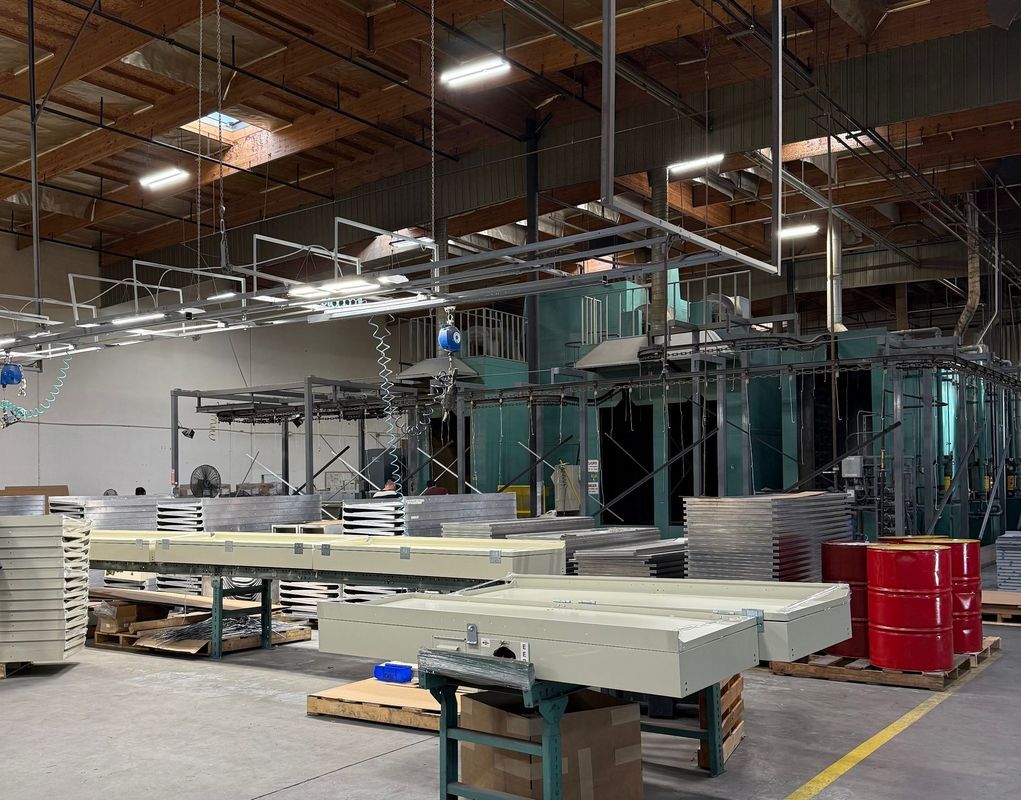 Warehouse interior with machinery, product on pallets, red barrels, and overhead metal structures.