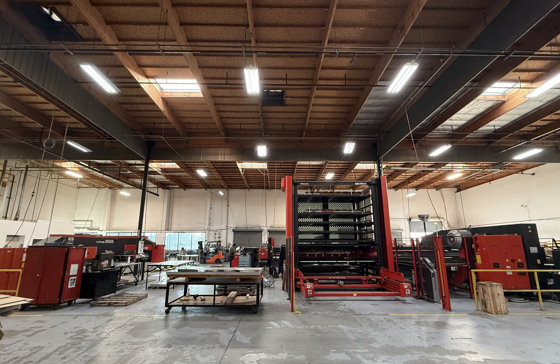 Inside of a warehouse, a large red machine in the center. Other machines and work areas are visible.