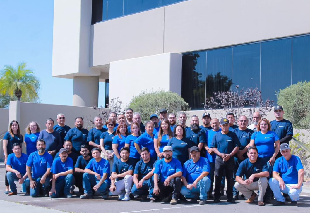 A large group of people in matching blue shirts standing together for a photo in front of a modern office building.