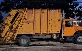 A yellow garbage truck is parked on the side of the road