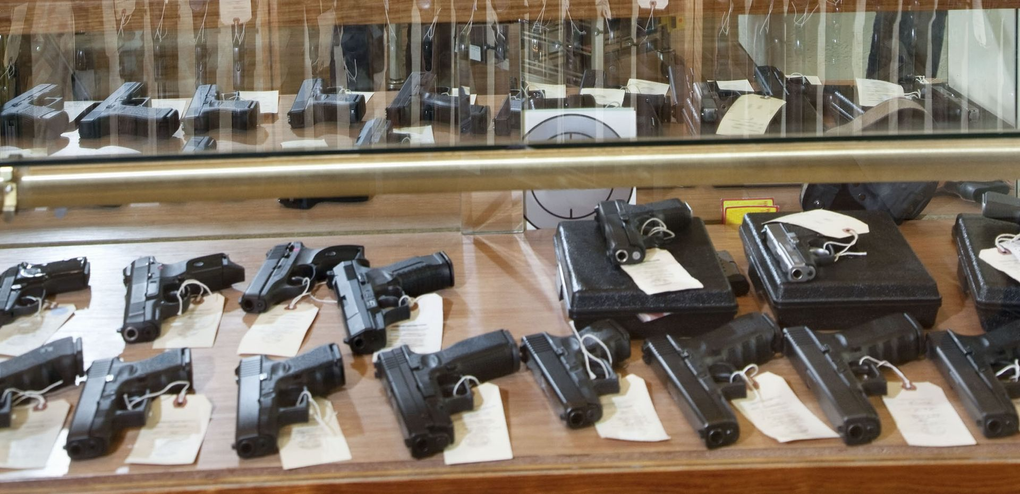 Guns displayed inside a glass case in what appears to be a gun store.