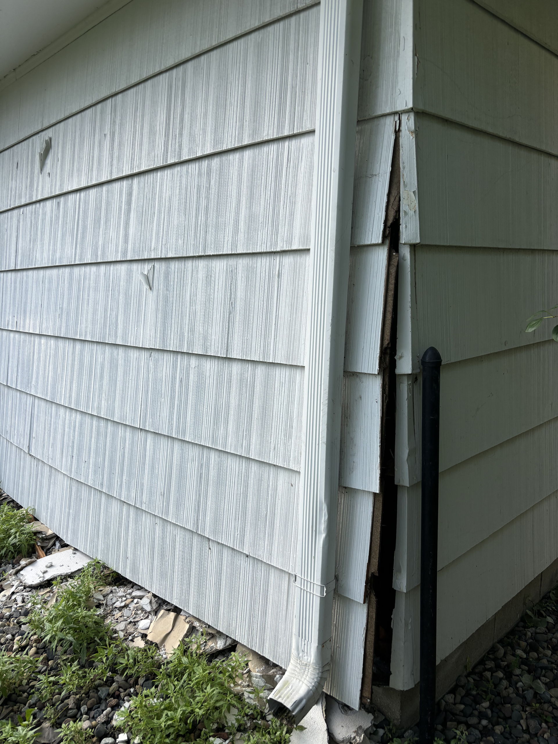 Damaged house siding with a large vertical split near the corner and exposed trim
