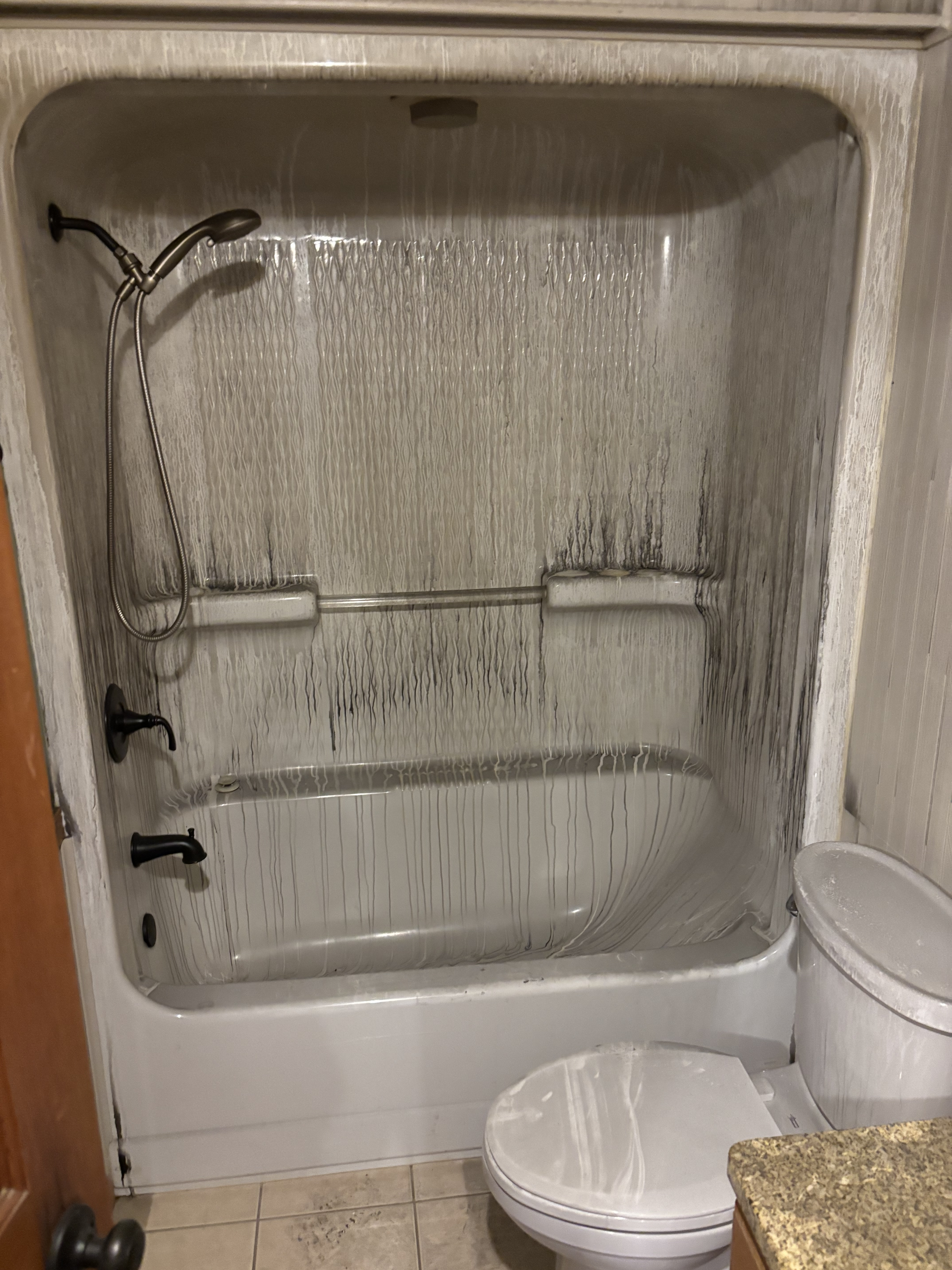 Shower stall with peeling wall surfaces, soap dish, and a bucket on the floor