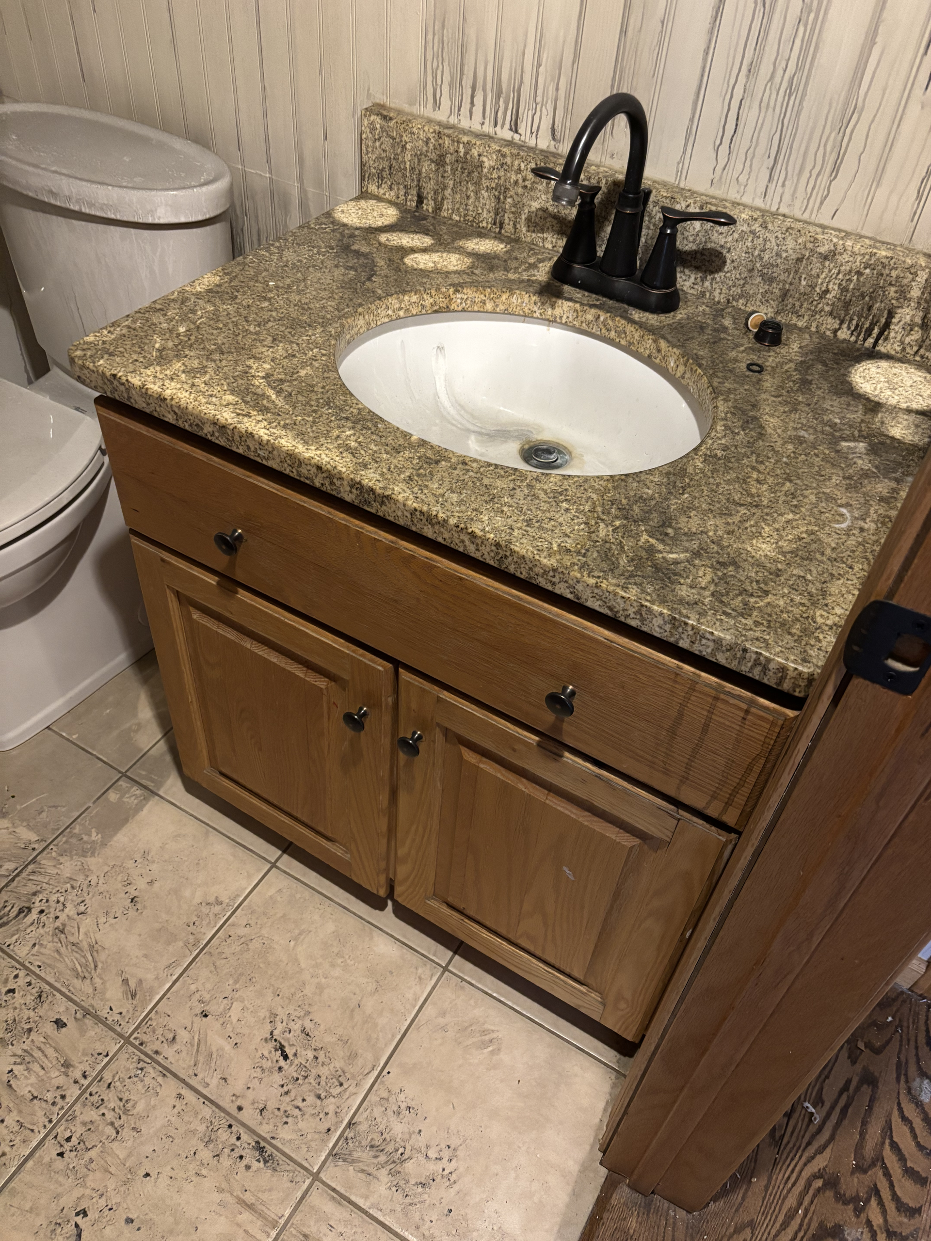 Bathroom vanity with granite countertop, white sink, and black faucet beside a toilet.