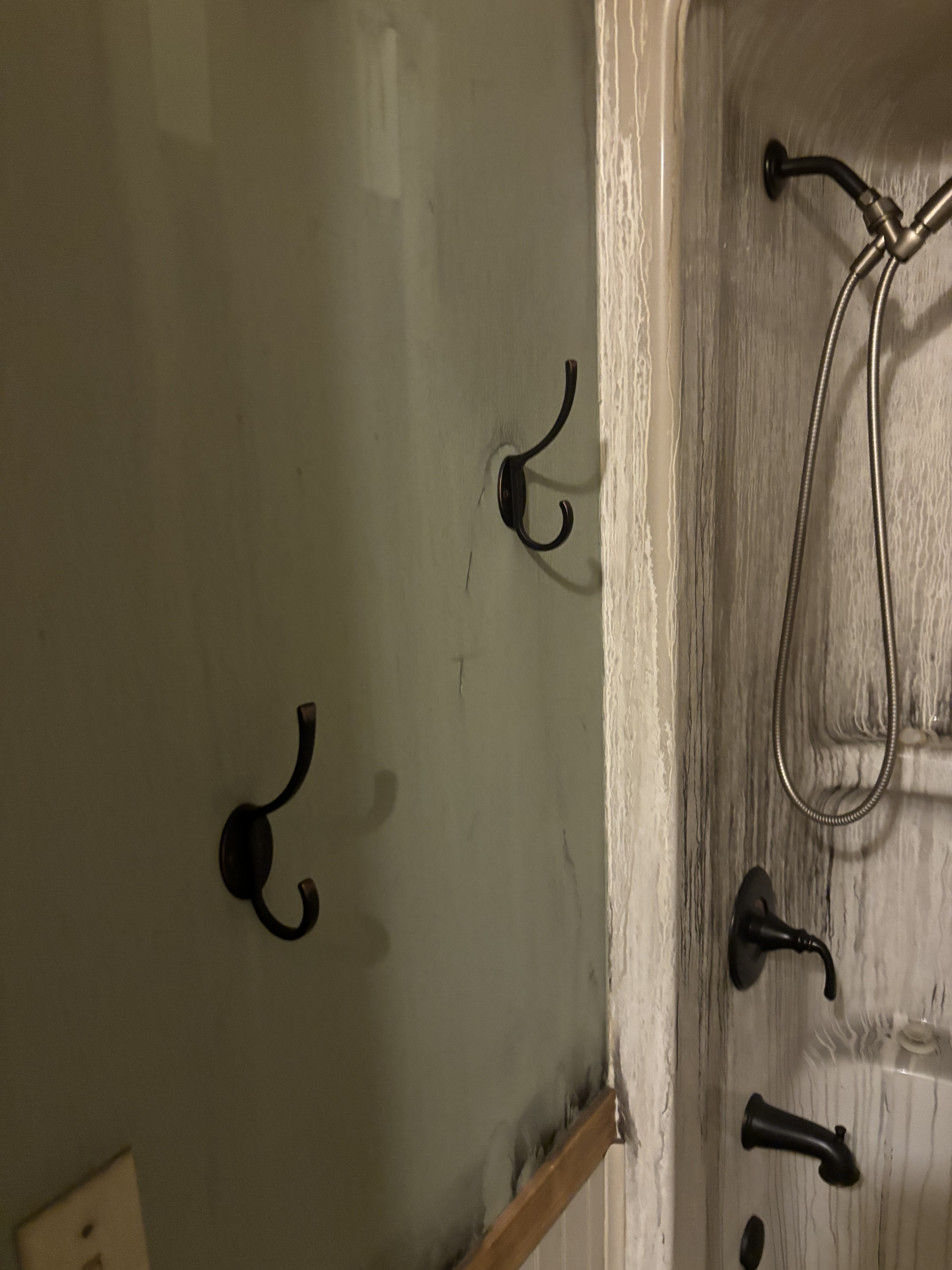 Unfinished shower wall with black hooks and plumbing fixtures beside a tiled corner