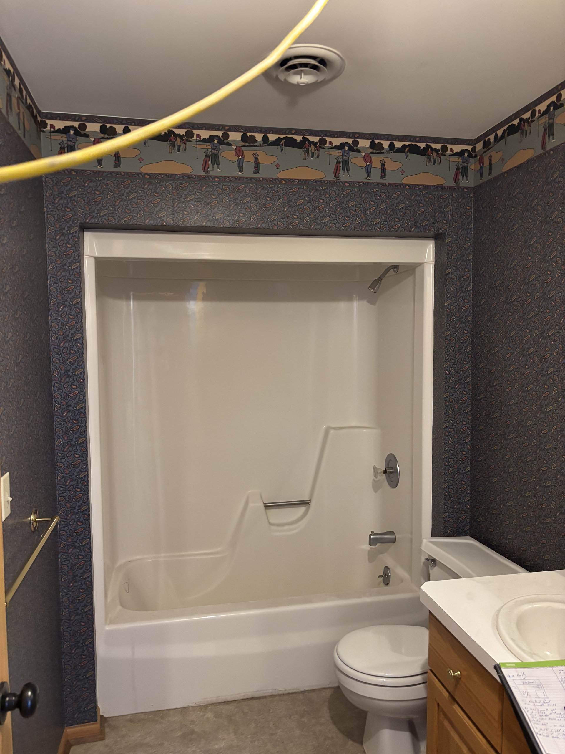 Bathroom with a white tub-shower, toilet, and vanity under renovation, with exposed wiring overhead.