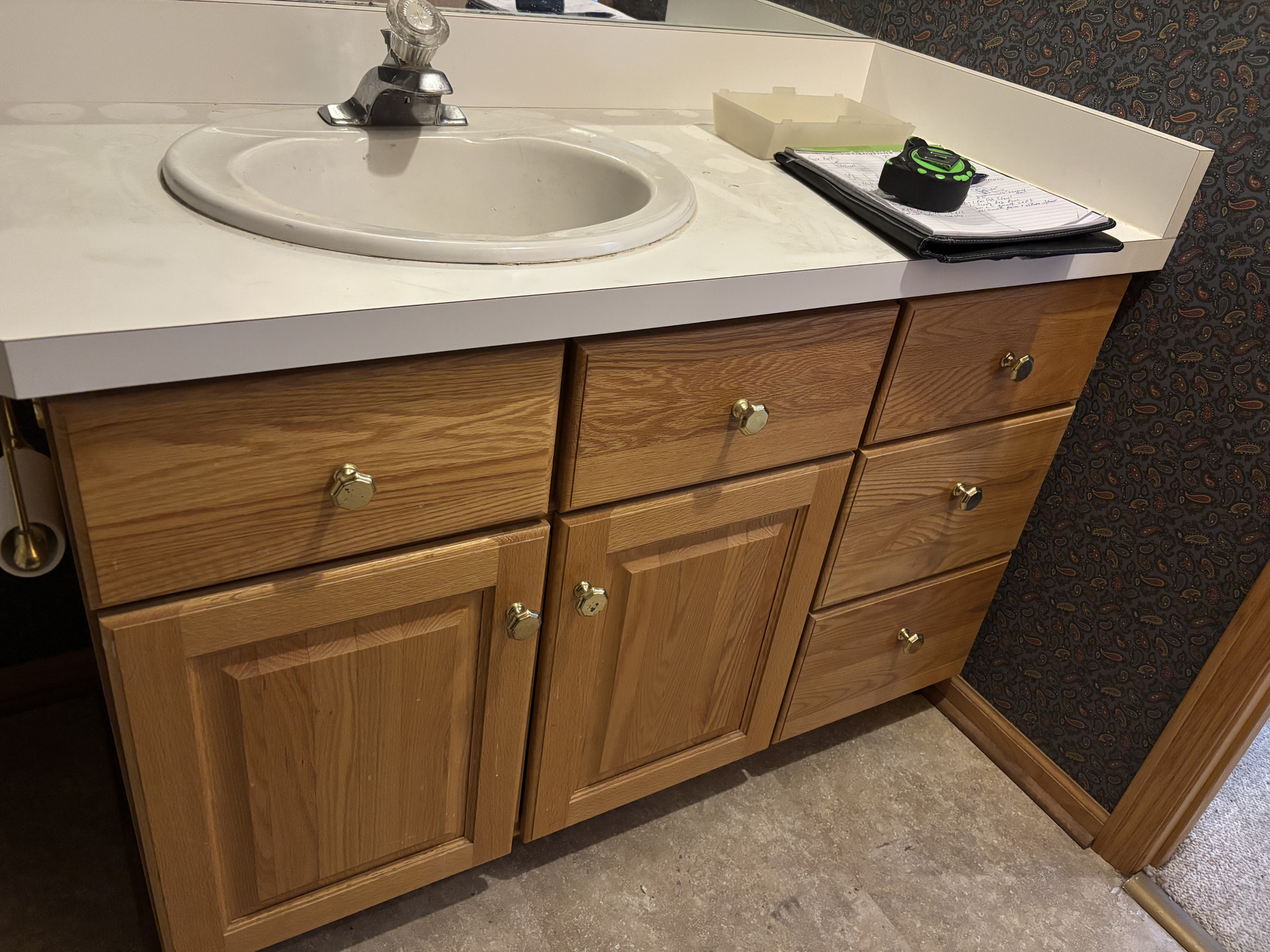 Bathroom vanity with sink and light wood cabinets, showing a towel, soap, and a textured wall corner.