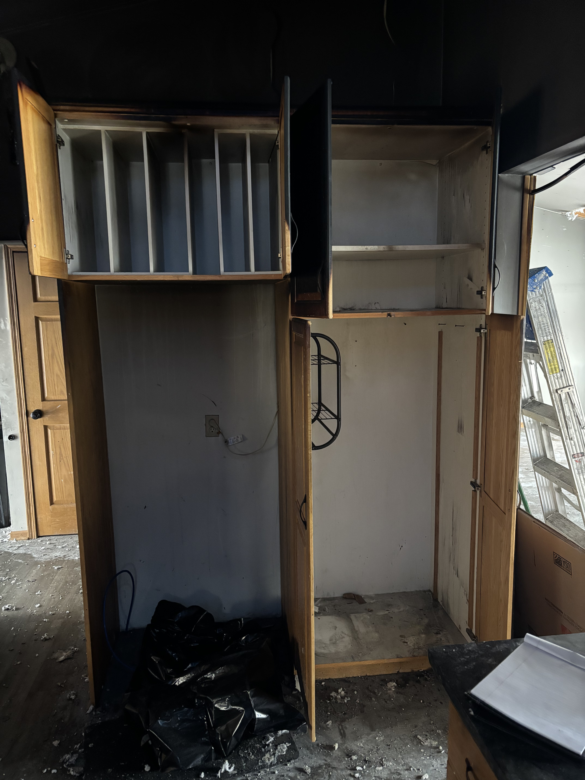 Damaged wooden cabinet with open compartments and exposed shelving in a cluttered, dim room.