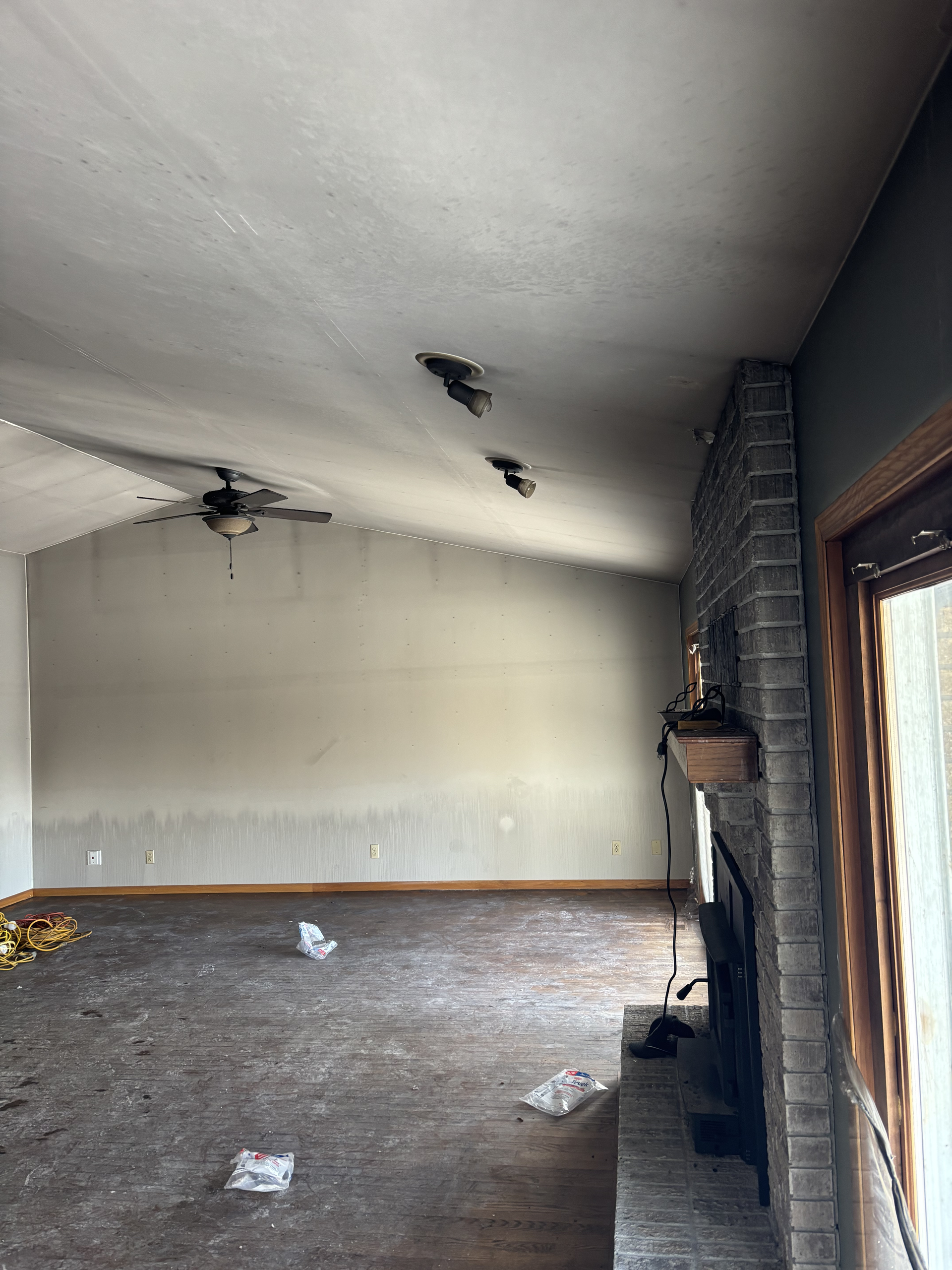 Damaged empty room with stained ceiling, exposed brick fireplace, and daylight from a window