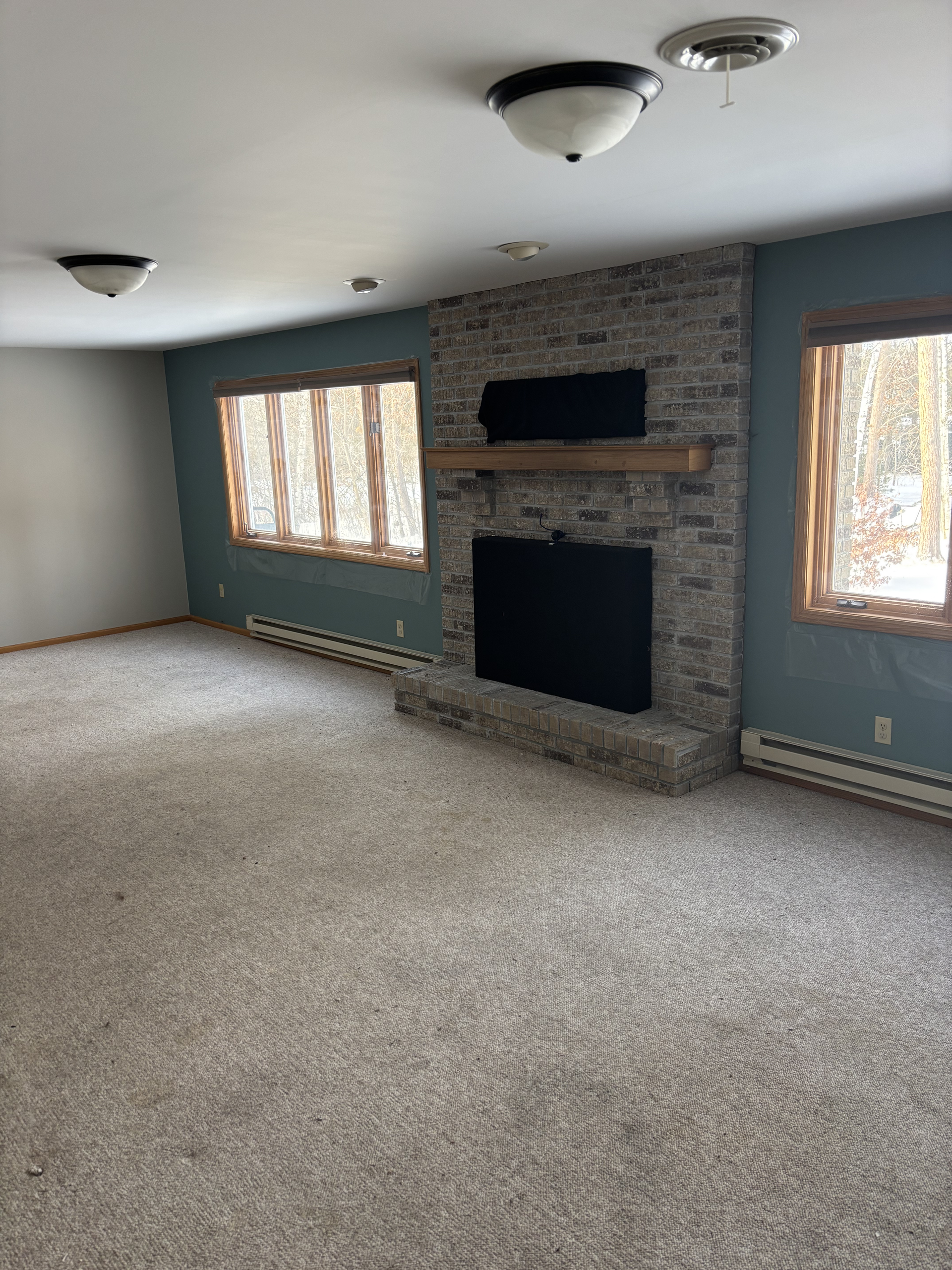Empty living room with carpet, brick fireplace, and windows on either side.