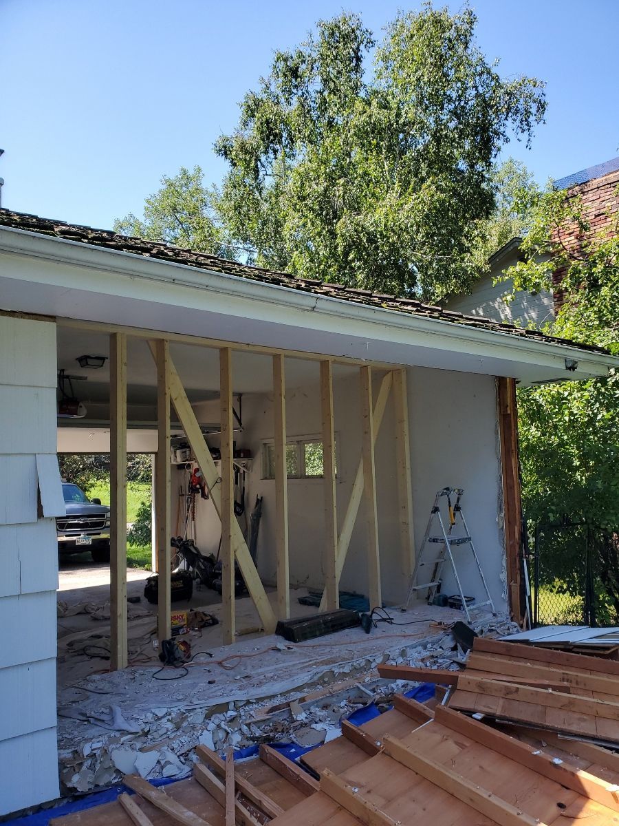 House under renovation with exposed framing and a ladder in a yard.