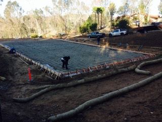 A large concrete slab is being poured into a dirt field.