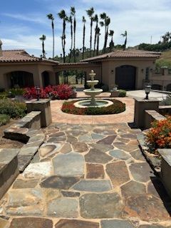 A stone walkway leading to a large house with a fountain in the middle.