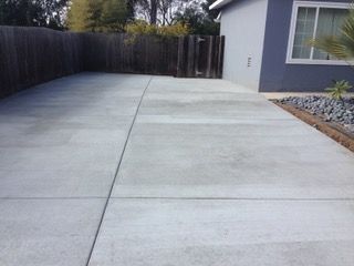 A concrete driveway leading to a house with a wooden fence.