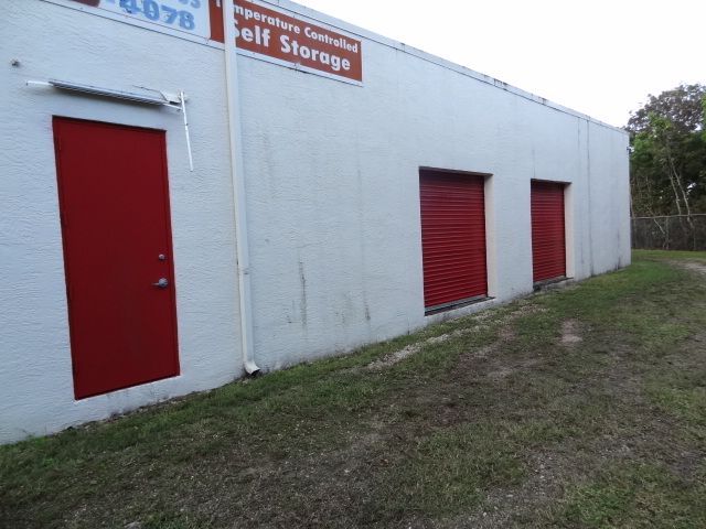 Exterior of a self-storage building with a red door and two red roll-up storage unit doors.