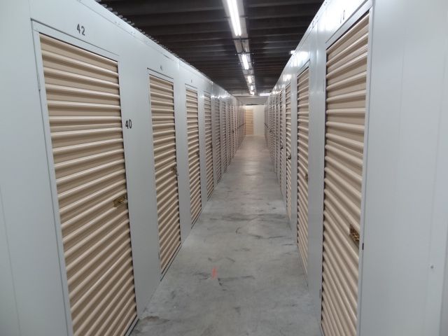 Interior view of storage units in a long hallway, with closed tan doors and overhead lighting.