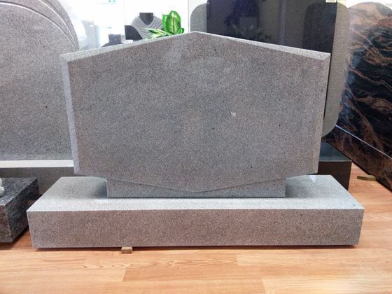 Gray granite memorial plaque with a pentagon-shaped top on a rectangular base in a cemetery setting