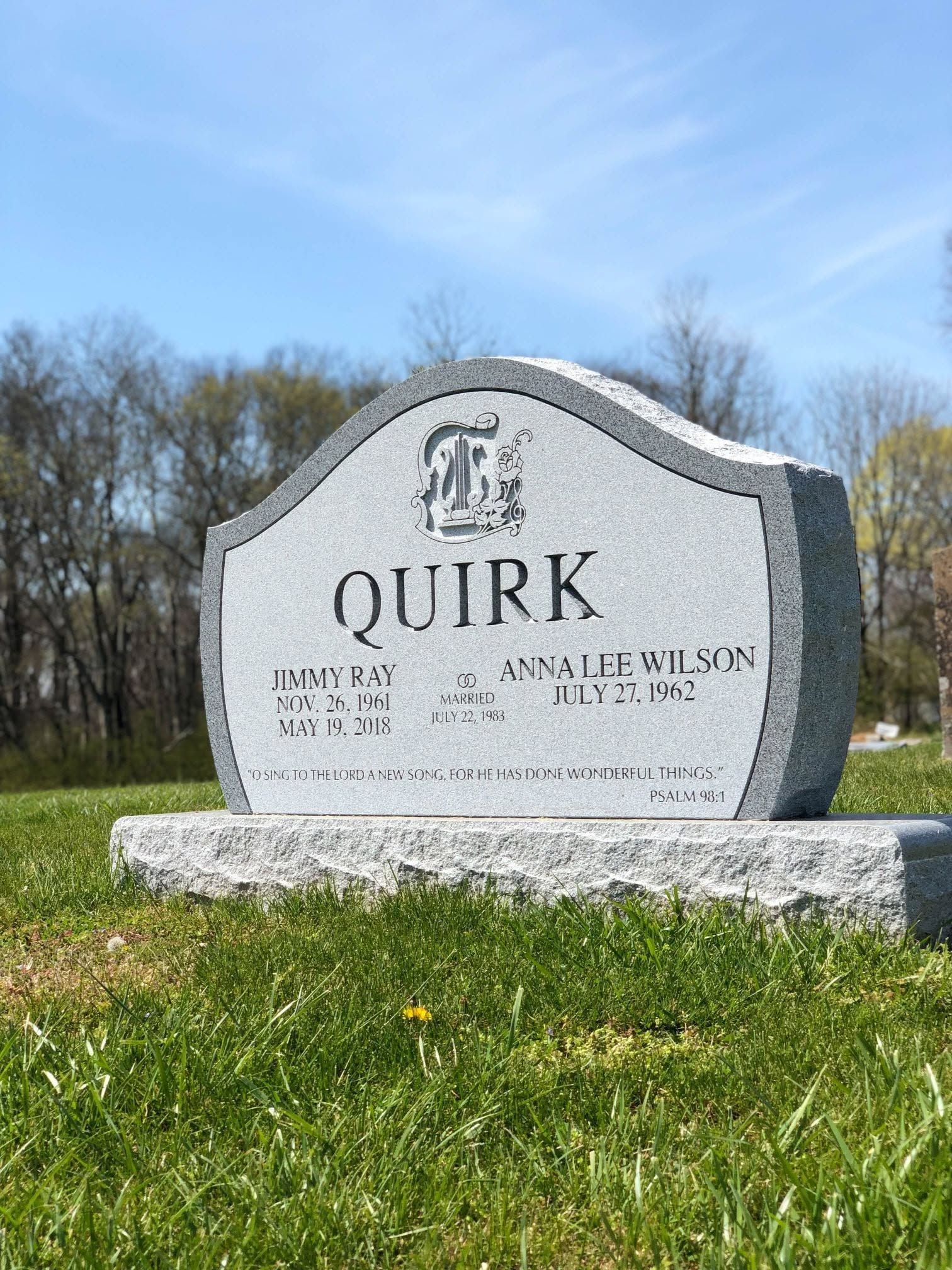 Gray Quirk headstone in a grassy cemetery under a blue sky