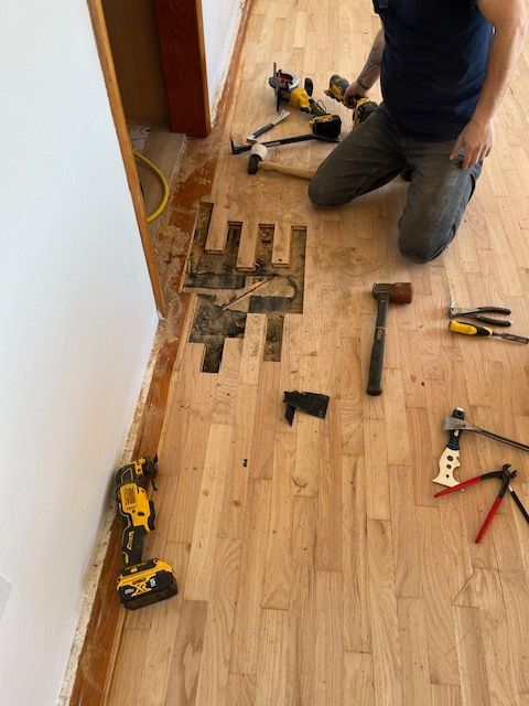 A man is kneeling on a wooden floor with tools