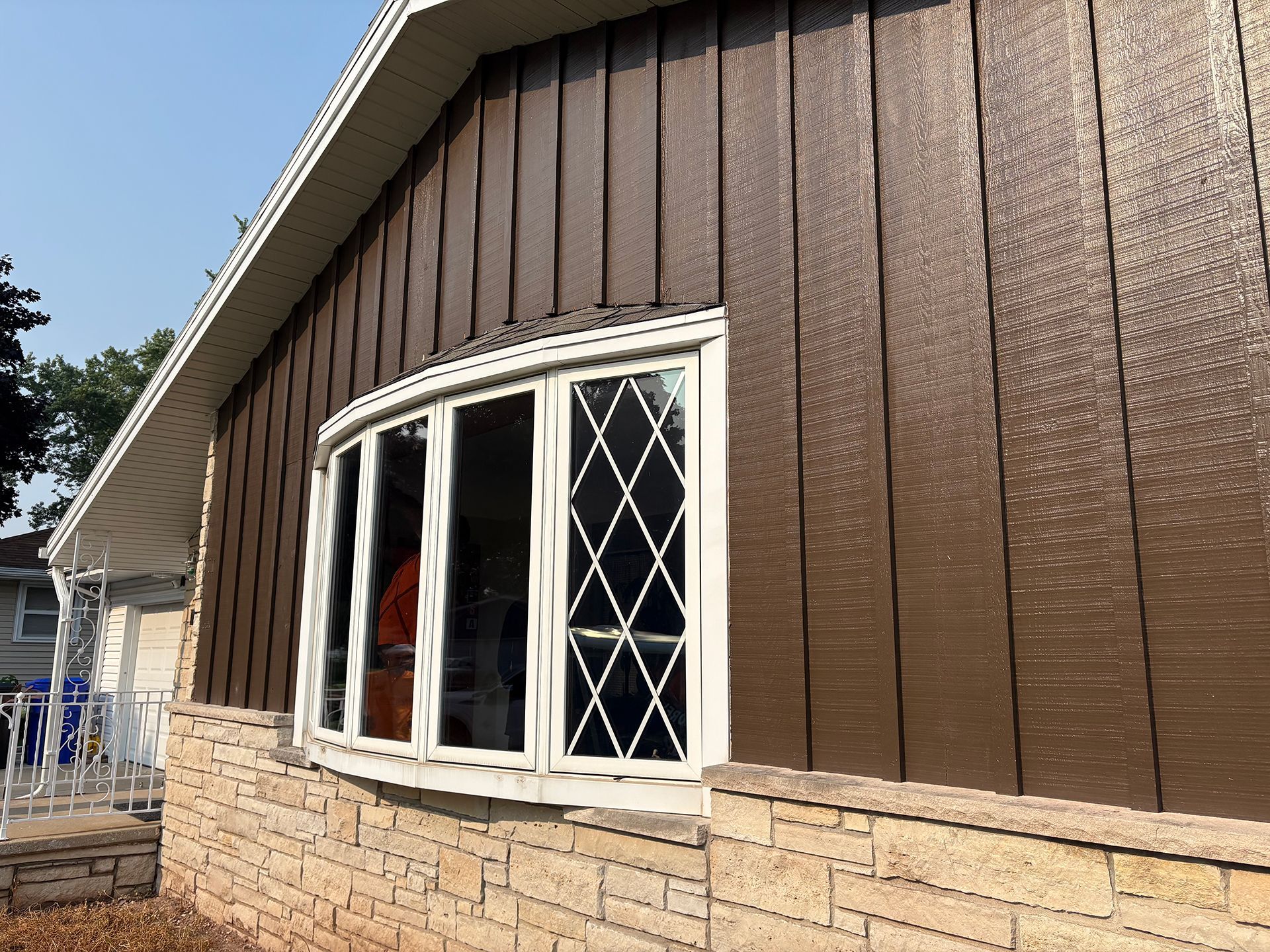 Brown siding with a bay window, stone base, and white trim on a house.