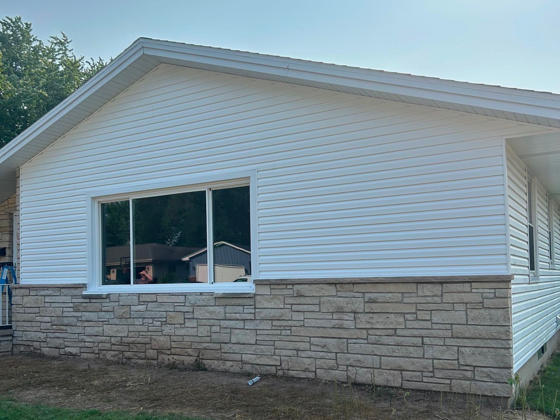 White-sided house with a large window and stone veneer base, under a blue sky.