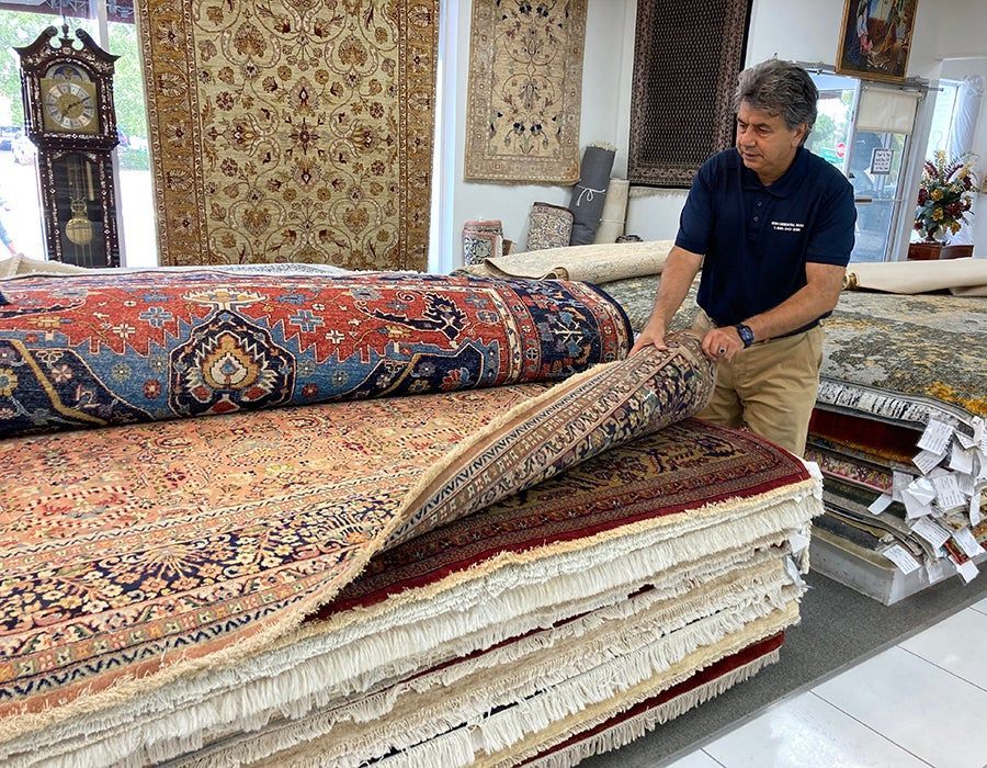 A man is standing next to a pile of rugs in a store.