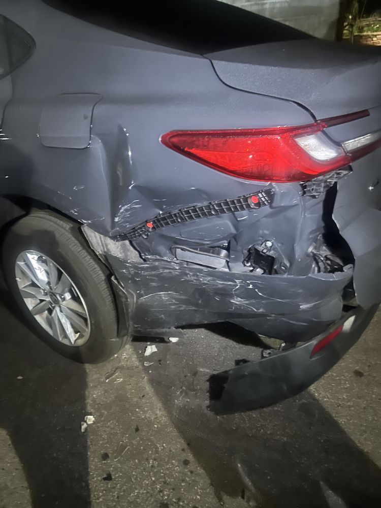 Rear of a gray sedan with severe right-side damage, broken bumper, and cracked taillight at night.