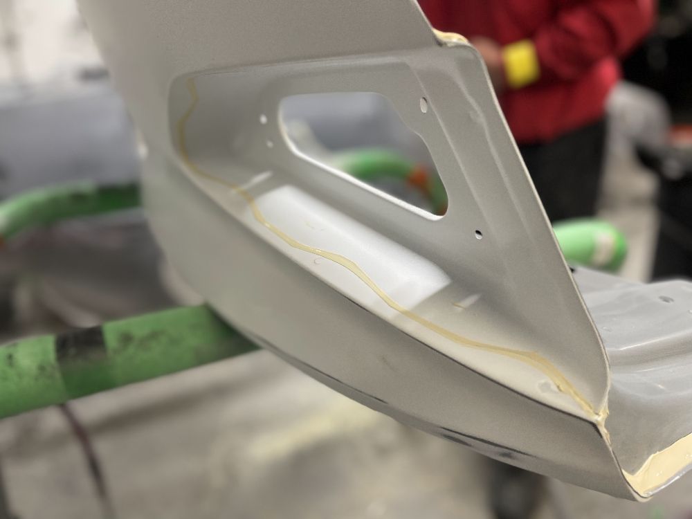 Close-up of a bent white metal car part with a cutout, resting on a green workbench.