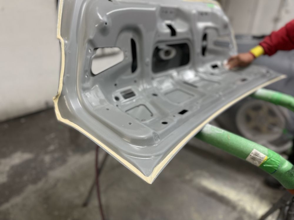 Car door panel being repaired in a workshop, with green support straps and a hand adjusting it.