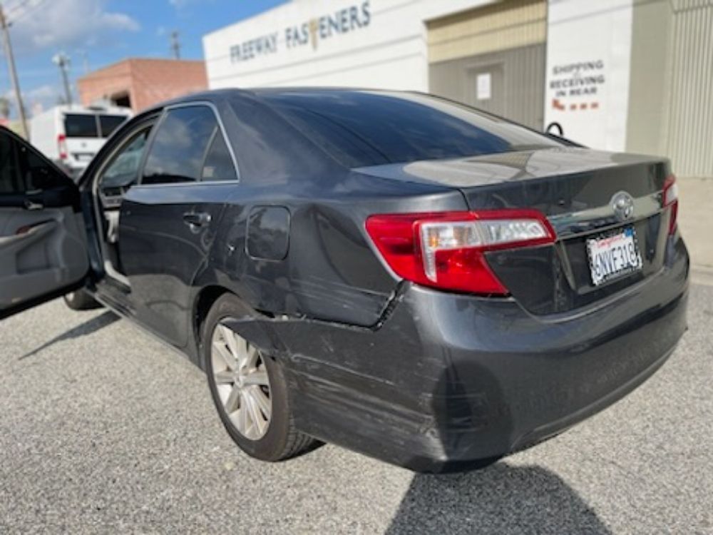 Black sedan with rear-end and side damage parked outside an auto repair shop.