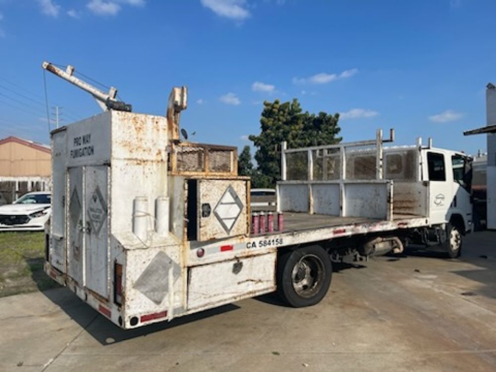 White utility truck with rusted service body parked on a lot under a blue sky.