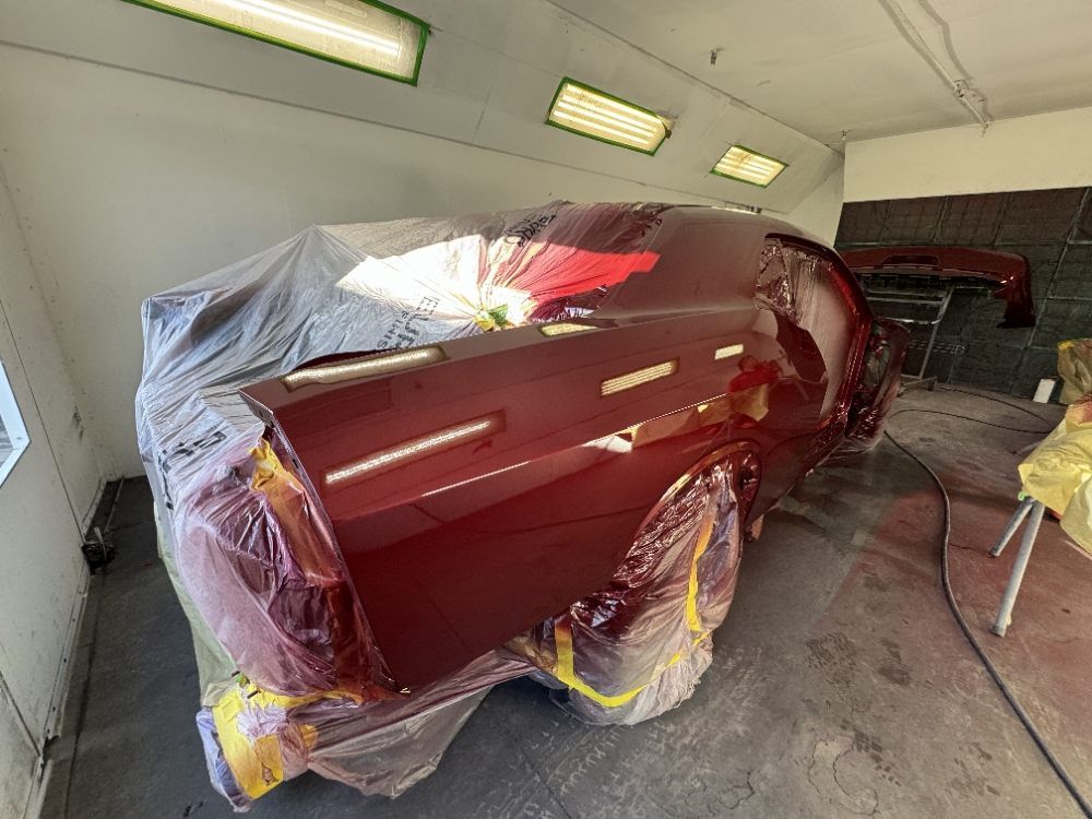 Red car body wrapped in plastic and masked for painting inside an auto body shop