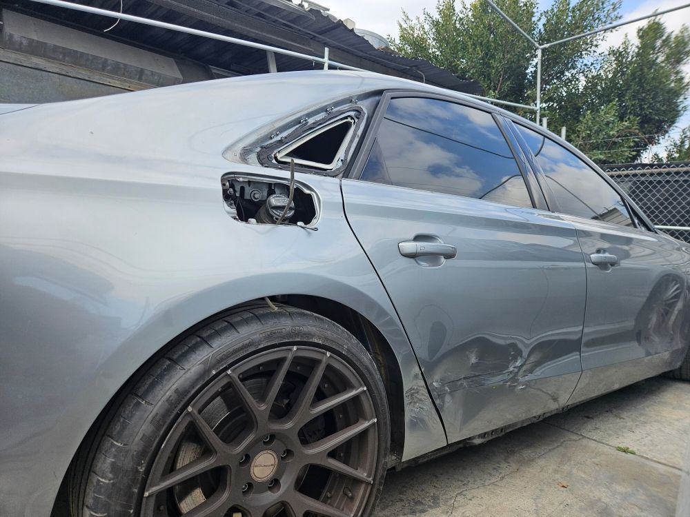 Gray sedan with damaged side and missing rear taillight, parked under a covered area