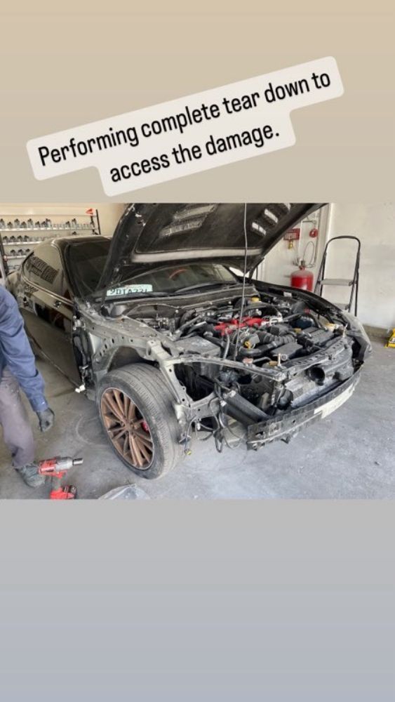 Car in repair shop with front end disassembled; caption says complete tear down to access damage.