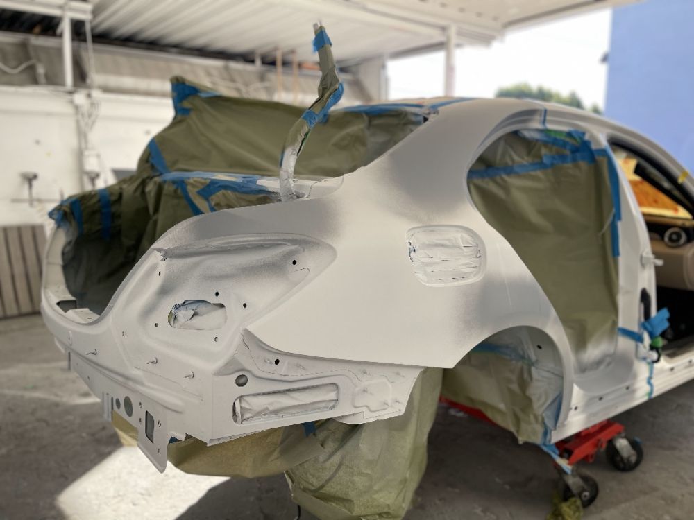 Car body in primer, masked with plastic and tape in an auto body repair shop