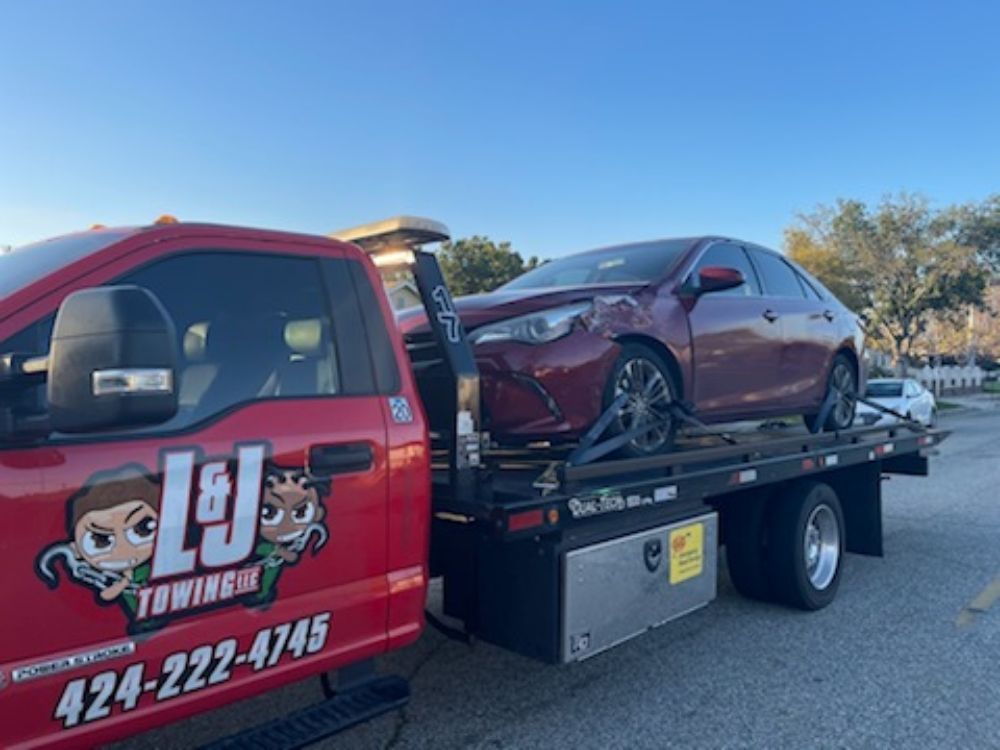 Red tow truck carrying a damaged maroon sedan on a flatbed trailer