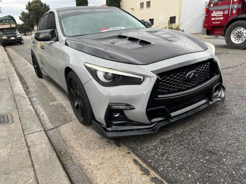 Damaged gray sports sedan parked at a curb with a dented front bumper and hood vents