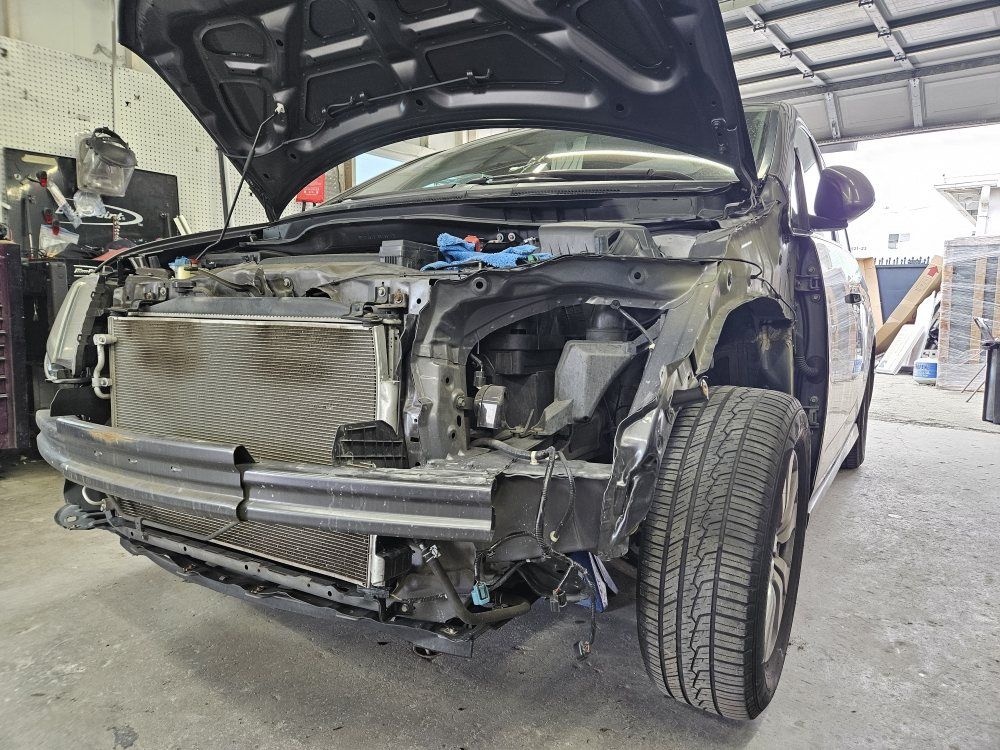 Damaged front end of a black car in a garage with hood open and exposed engine parts