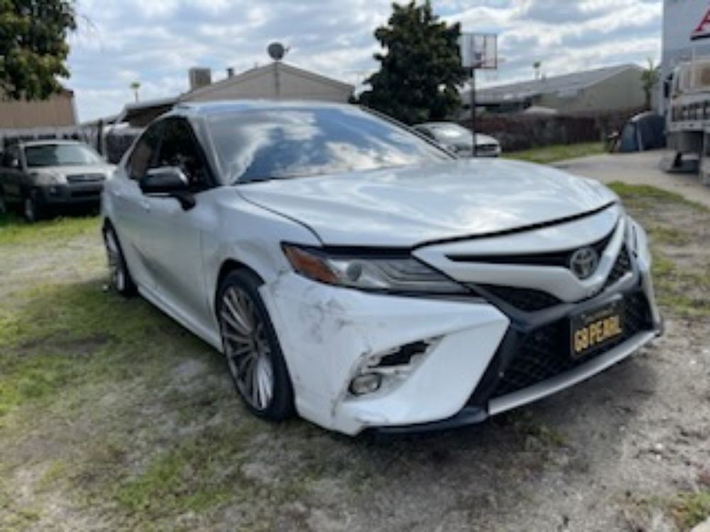 White Toyota Camry parked on a grassy lot with a black front grille and damage on the front bumper