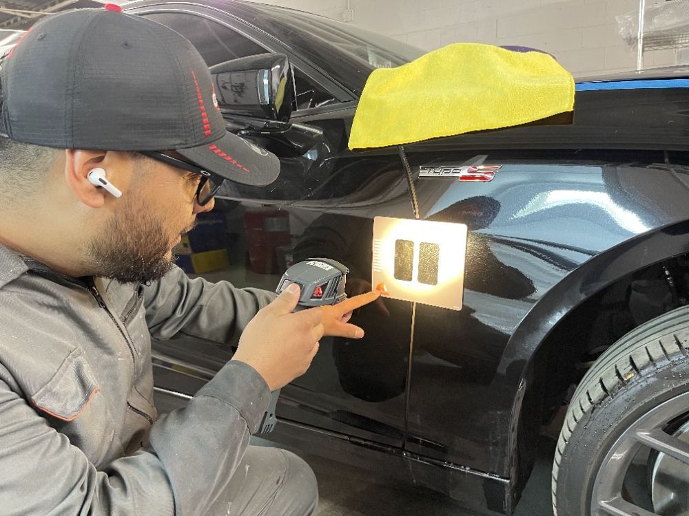 Technician inspecting a black car door with a handheld light in a workshop