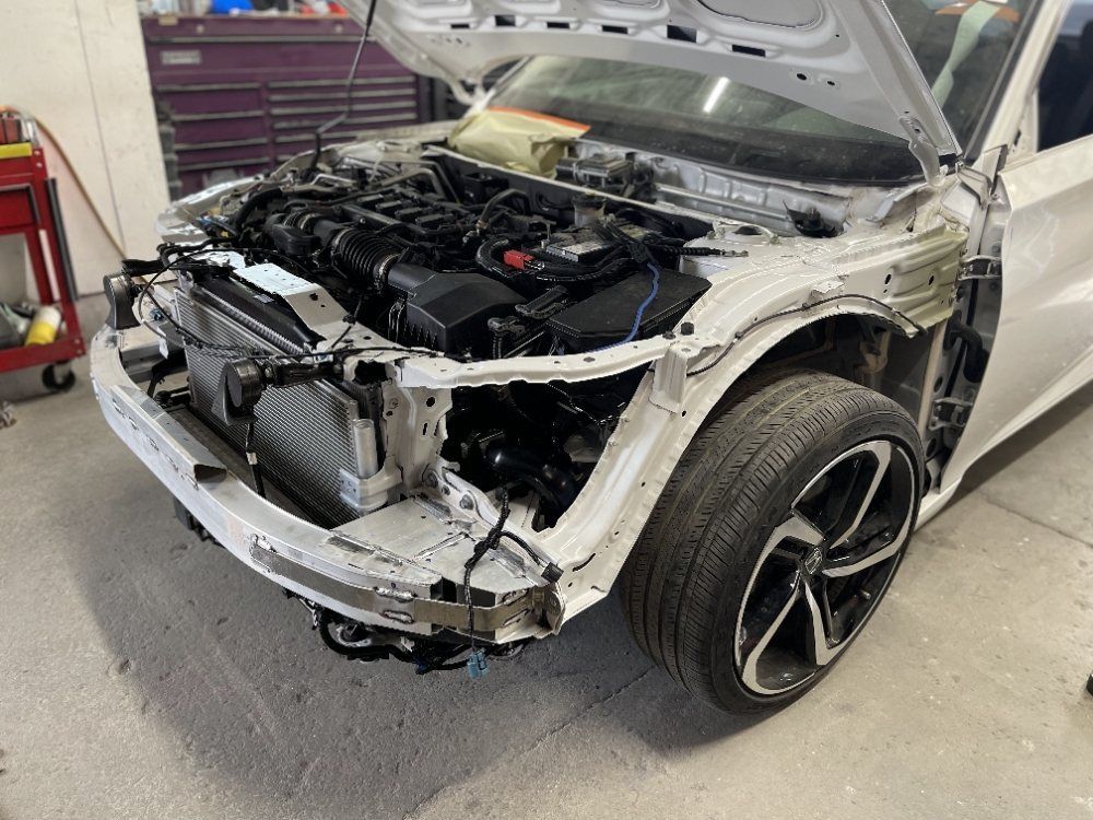 Damaged white car in a repair shop, front end stripped and hood open