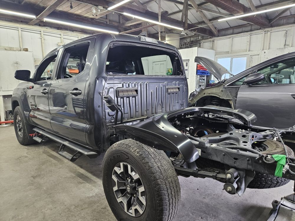 Damaged dark pickup truck in a repair shop with front end removed and exposed frame