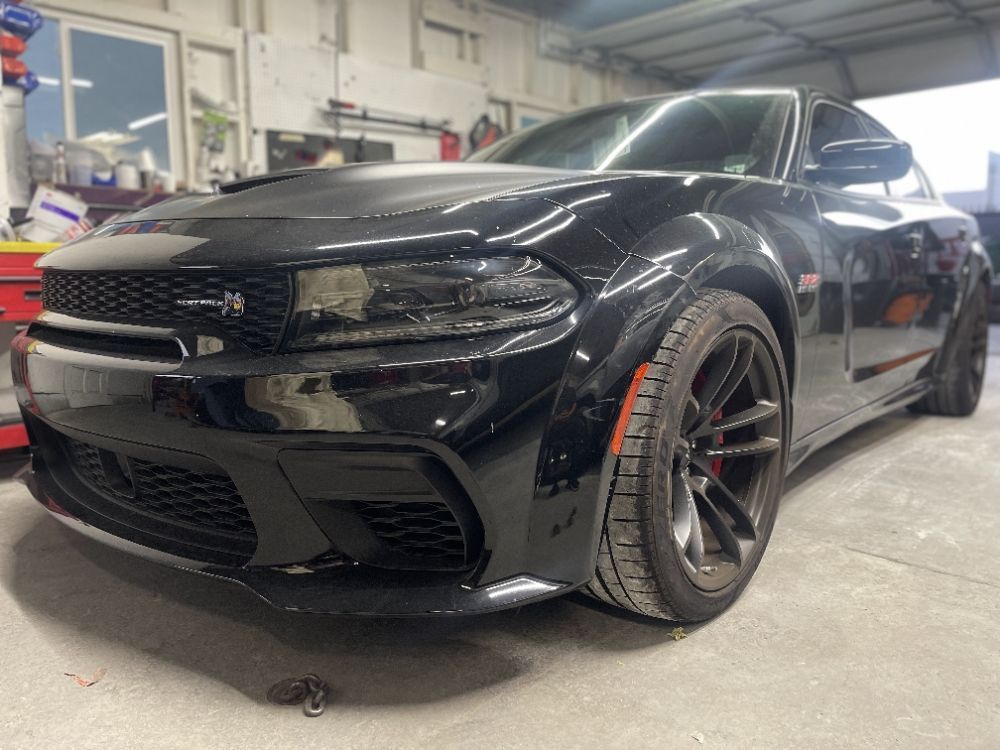 Black Dodge Charger in a garage, front three-quarter view on a lift with red brake calipers.