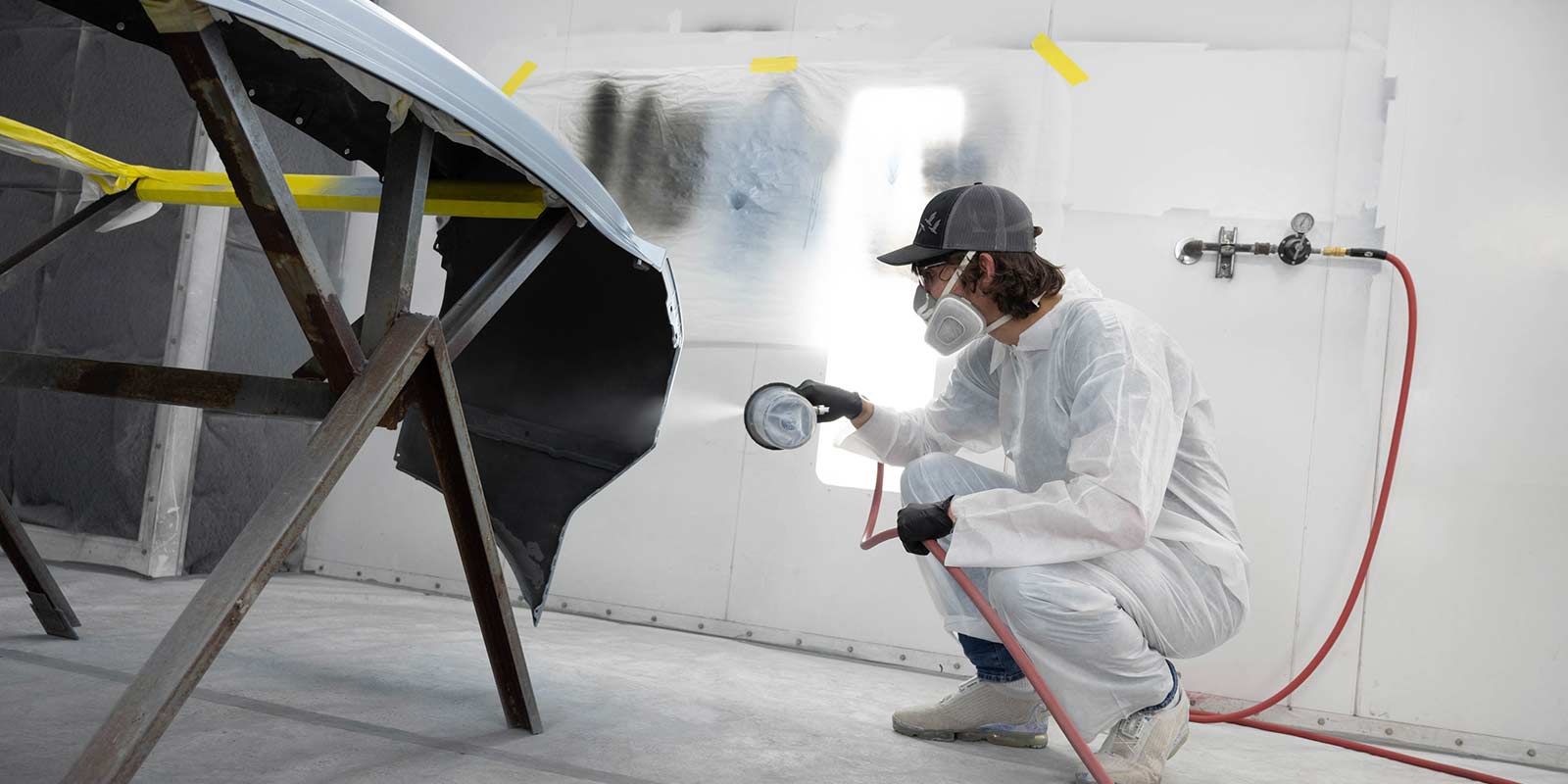 Worker in white protective suit spray-painting a metal chair in a bright workshop